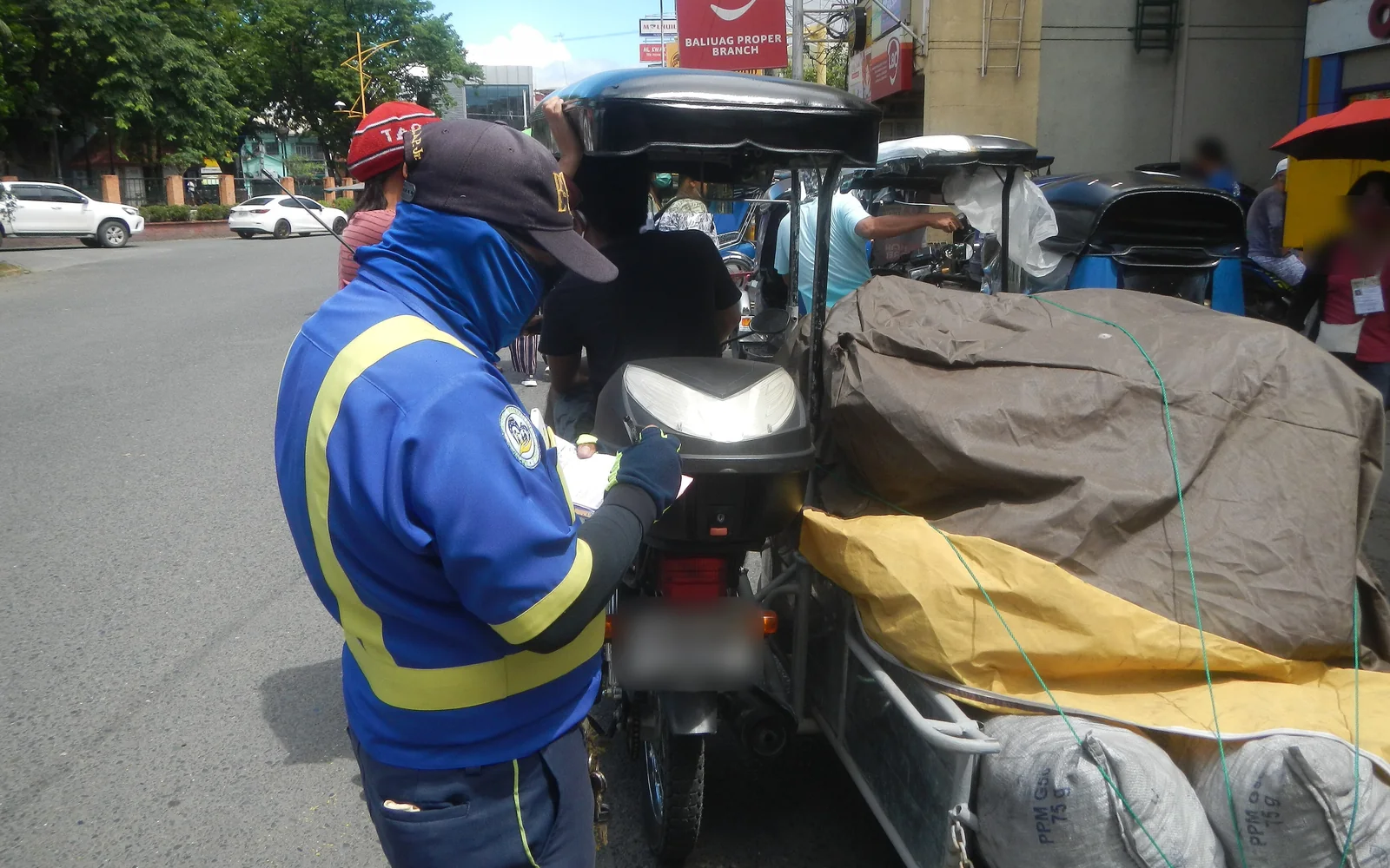 A traffic enforcer writing a paper citation by hand behind a parked tricycle